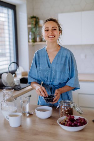 Foto de Mujer joven preparando un muesli para el desayuno en su cocina, rutina de la mañana y el concepto de estilo de vida saludable. - Imagen libre de derechos