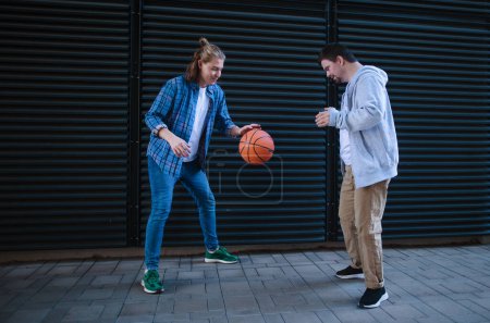 Téléchargez les photos : Homme avec le syndrome du duvet jouant au basket en plein air avec son ami. Concept d'amitié et d'intégration des personnes handicapées dans la société. - en image libre de droit