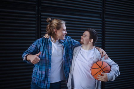 Téléchargez les photos : Homme avec le syndrome du duvet jouant au basket en plein air avec son ami. Concept d'amitié et d'intégration des personnes handicapées dans la société. - en image libre de droit