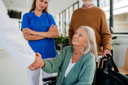 Foto de Mujer mayor en silla de ruedas reuniéndose con un médico en el hospital, estrechando las manos. - Imagen libre de derechos