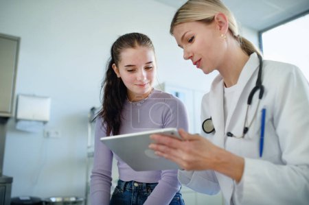 Photo for Young woman doctor explaining diagnosis to teenage girl in her ambulance office. - Royalty Free Image