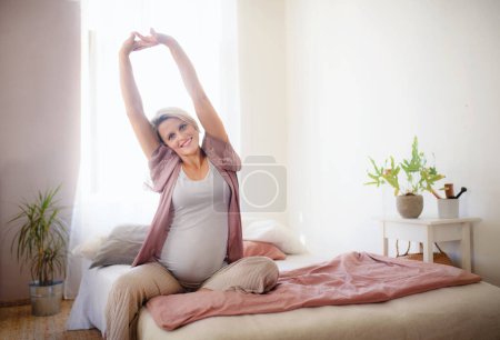 Photo for Pregnant woman sitting and stretching on a bed. - Royalty Free Image