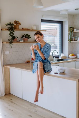 Foto de Mujer joven disfrutando de una taza de café por la mañana, en una cocina. - Imagen libre de derechos
