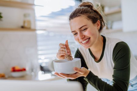 Photo for Young woman having a muesli for breakfast in her kitchen, morning routine and healthy lifestyle concept. - Royalty Free Image
