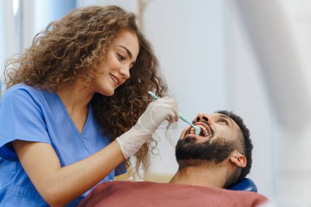 Foto de Mujer joven dentista haciendo un examen preventivo al hombre multirracial. - Imagen libre de derechos