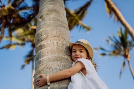 Foto de Niña feliz abrazando la palmera durante las vacaciones tropicales. - Imagen libre de derechos