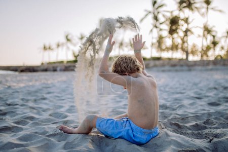 Téléchargez les photos : Vue arrière du petit garçon ludique jouant avec le sable sur la plage. - en image libre de droit