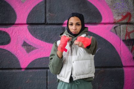 Foto de Retrato de joven musulmana con guantes deportivos, de pie frente a un graffiti. - Imagen libre de derechos