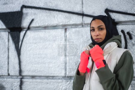 Téléchargez les photos : Portrait de jeune femme musulmane avec des gants de sport, debout devant un graffiti. - en image libre de droit