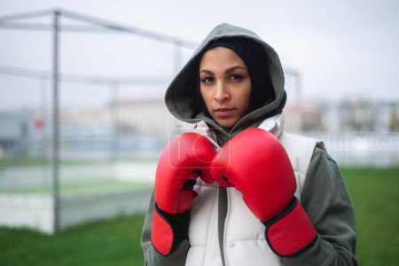 Téléchargez les photos : Portrait d'une jeune femme musulmane avec des gants de boxe debout à l'extérieur. - en image libre de droit