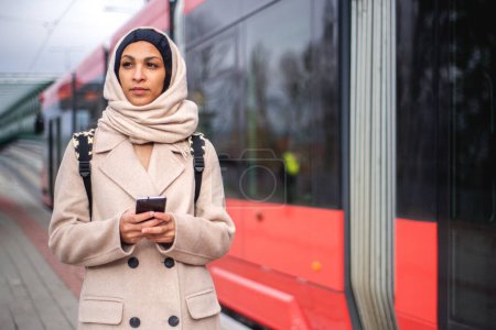 Téléchargez les photos : Jeune femme musulmane avec smartphone sortant d'un tram. - en image libre de droit