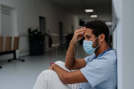 Photo for Young distressed doctor sitting at a hospital corridor floor. - Royalty Free Image