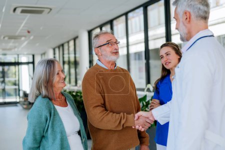 Photo for Mature doctor and his young colleaguetalking with his senior patients at hospital corridor. - Royalty Free Image