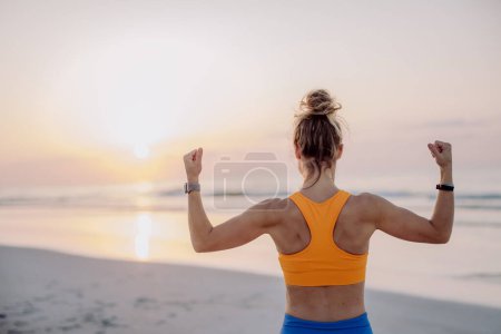 Photo for Rear view of young woman taking exercises at the beach, morning routine and healthy lifestyle concept. - Royalty Free Image