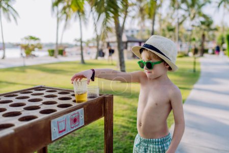 Photo for Little boy putting down his drink at storage table on a beach. - Royalty Free Image