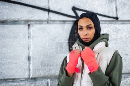 Téléchargez les photos : Portrait de jeune femme musulmane avec des gants de sport, debout devant un graffiti. - en image libre de droit
