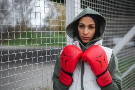 Téléchargez les photos : Portrait d'une jeune femme musulmane avec des gants de boxe debout à l'extérieur. - en image libre de droit
