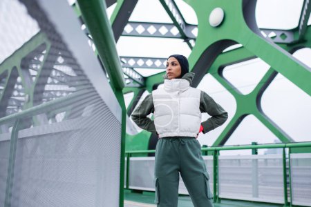 Téléchargez les photos : Jeune femme musulmane se reposant après le jogging, en plein air dans une ville. - en image libre de droit