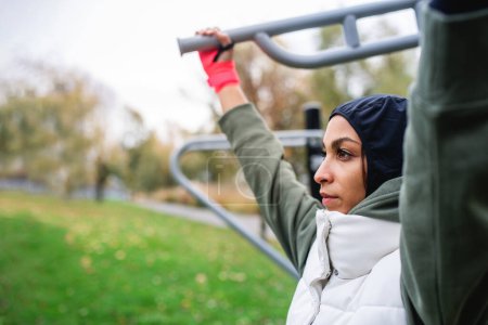 Téléchargez les photos : Jeune femme musulmane dans un hijab sportif faisant de l'exercice dans un terrain d'entraînement en plein air. - en image libre de droit