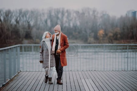 Photo for Elegant senior couple walking near a river, during cold winter day. - Royalty Free Image