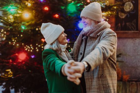 Senioren-Paar verbringt romantische Zeit auf dem Weihnachtsmarkt im Freien und tanzt neben einem Weihnachtsbaum.