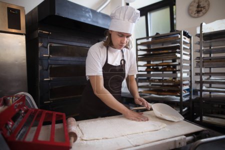Téléchargez les photos : Jeune boulanger avec casquette de chef préparant des pâtisseries dans une boulangerie. - en image libre de droit
