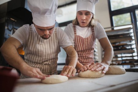 Téléchargez les photos : L'homme au syndrome du duvet aide à préparer le pain dans une boulangerie avec son collègue. Concept d'intégration des personnes handicapées dans la société. - en image libre de droit