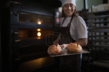 Photo for Happy young baker with fresh bread, in a bakery. - Royalty Free Image