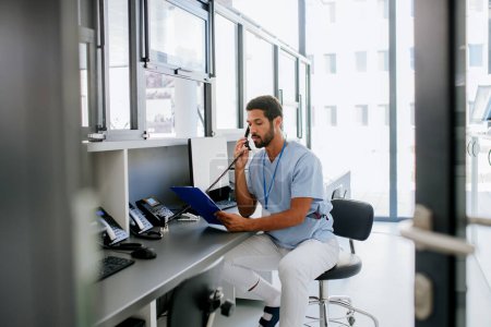 Téléchargez les photos : Young multiracial doctor sitting in his office and calling. - en image libre de droit