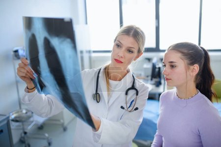 Mujer joven médico que muestra imagen de rayos X de los pulmones a la paciente.