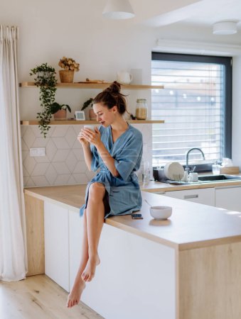 Téléchargez les photos : Jeune femme dégustant une tasse de café le matin, dans une cuisine. - en image libre de droit