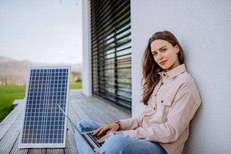 Foto de Mujer joven sentada en la terraza, cargando la tableta a través del panel solar. - Imagen libre de derechos