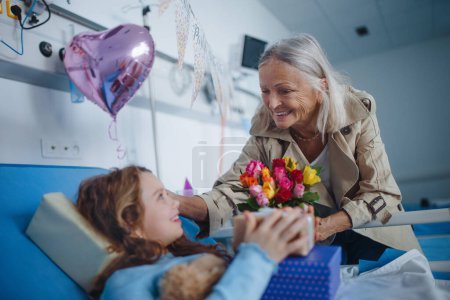 Téléchargez les photos : Granmother visiting her sick granddaughter in a hospital, celebrating her birthday. - en image libre de droit