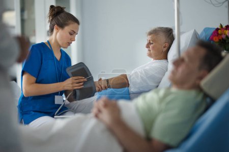 Téléchargez les photos : Jeune infirmière mesurant la pression artérielle chez un patient âgé. - en image libre de droit