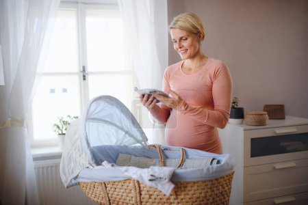 Téléchargez les photos : Heureuse femme enceinte regardant des petits vêtements de bébé. - en image libre de droit