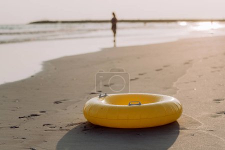 Photo for Close-up of yellow inflatable wheel on the beach, with person in the background. - Royalty Free Image