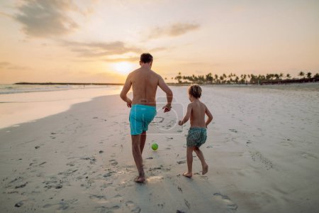 Photo for Rear view of father with his son plaing football on a beach. - Royalty Free Image
