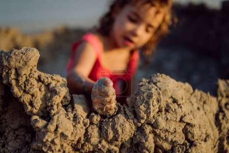 Photo for Little girl playing on the beach, digging hole in the sand. - Royalty Free Image
