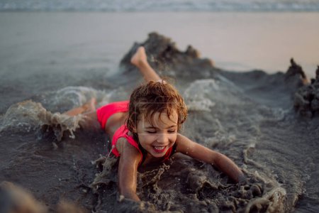 Foto de Niña jugando en la playa, cavando hoyos en la arena. - Imagen libre de derechos