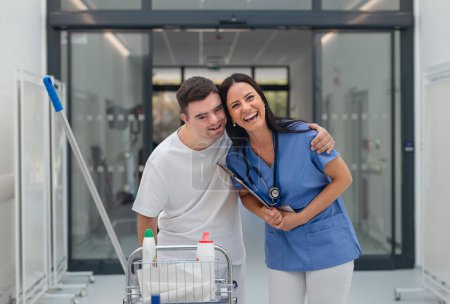 Téléchargez les photos : Young man with down syndrome working in hospital as cleaner, talking to nurse, having fun. Concpet of integration people with disability into society. - en image libre de droit