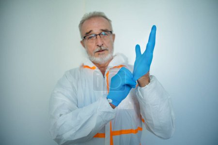Foto de Portrait of doctor in a protective coveral putting on surgical gloves. - Imagen libre de derechos