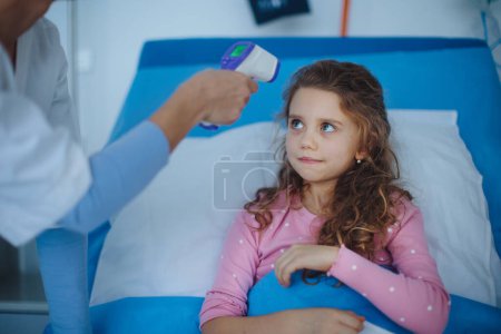 Téléchargez les photos : Nurse measuring body temperature to little girl lying in a hospital. - en image libre de droit