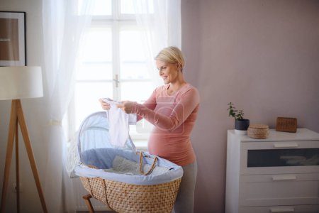 Téléchargez les photos : Heureuse femme enceinte regardant des petits vêtements de bébé. - en image libre de droit
