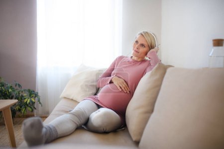 Foto de Mujer embarazada sentada en una cama, escuchando música y disfrutando del tiempo para ella. - Imagen libre de derechos