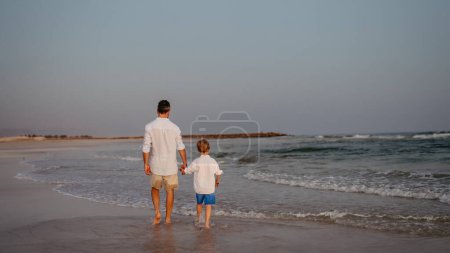 Foto de Rear view of father and his son walking on the beach, enjoying exotic vacation. - Imagen libre de derechos