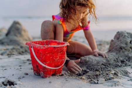 Téléchargez les photos : Little girl playing on the beach, building a sand castle. - en image libre de droit