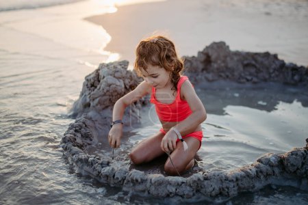 Foto de Niña jugando en la playa, cavando hoyos en la arena. - Imagen libre de derechos