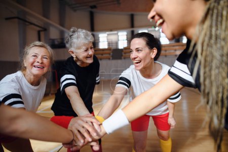 A group of multigenerational women in gym stacking hands together, sport team players.