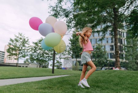 Foto de Portrait of little blond girl posing with baloons in city and looking at camera. - Imagen libre de derechos