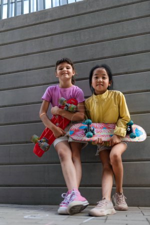 Photo for Happy friends posing together in city, standing in front of a concrete wall, holding skateboards and looking at camera. - Royalty Free Image